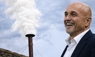 Spalletti sorridente di fianco ad un comignolo con una fumata bianca, immagine creata con intelligenza artificiale